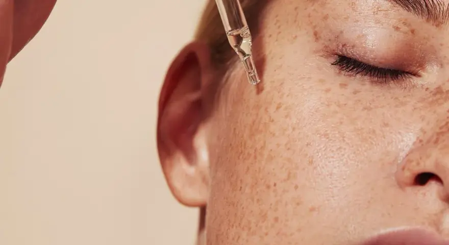 Kropla serum z pipety spada na piegowatą skórę. Czy to retinol? Co to jest retinol i jak działa?