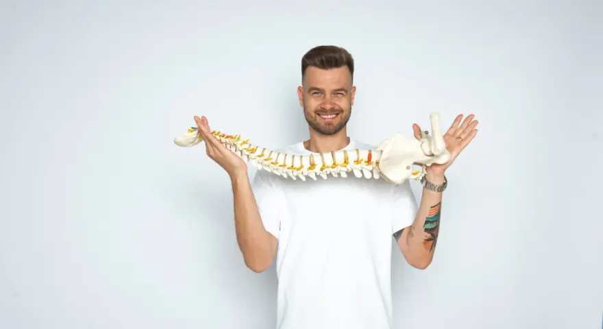 Uśmiechnięty mężczyzna trzyma model kręgosłupa, jakby prezentował jego elastyczność, niczym worek oponowy.