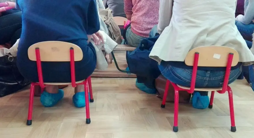 Dostateczny, jaka to ocena? Dzieci siedzą na małych krzesełkach w niebieskich ochraniaczach na buty.