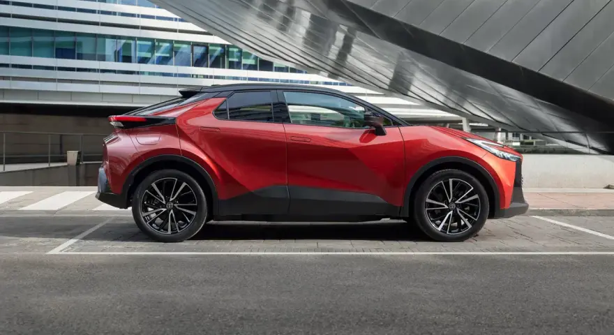 Czerwona Toyota C-HR Hybrid na tle nowoczesnego budynku. Zastanawiasz się, ile kosztuje Toyota C-HR Hybrid?