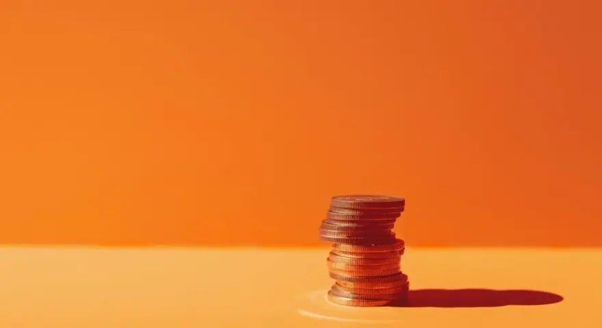 A stack of coins on an orange surface, symbolizing the business account requirements for financial growth.