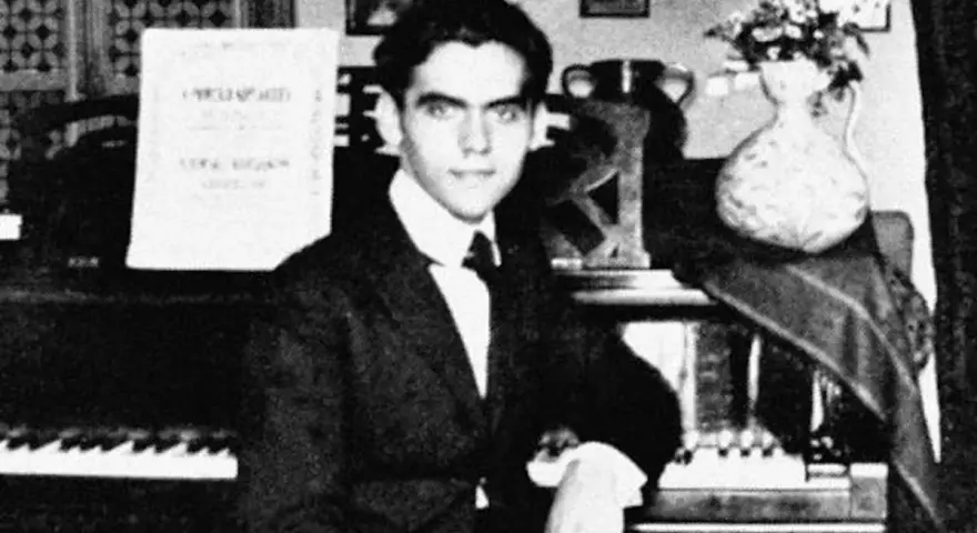 Ung man vid piano, kanske Federico García Lorca, med noter och blommor i vas.