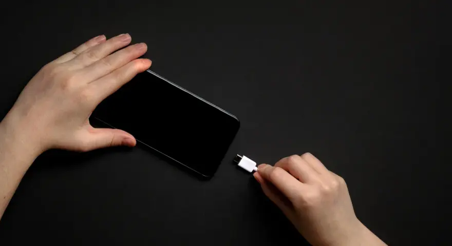 Dwie dłonie trzymają smartfon i biały kabel USB-C. Zastanawiasz się, do ilu procent ładować telefon, by zadbać o jego baterię?