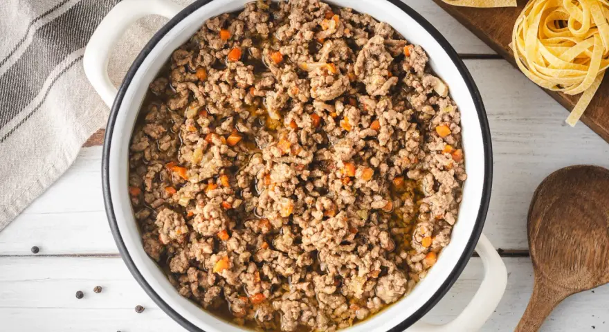 Un saporito ragù bianco in una pentola, pronto per condire la pasta. Pezzetti di carota e cipolla si mescolano alla carne macinata.