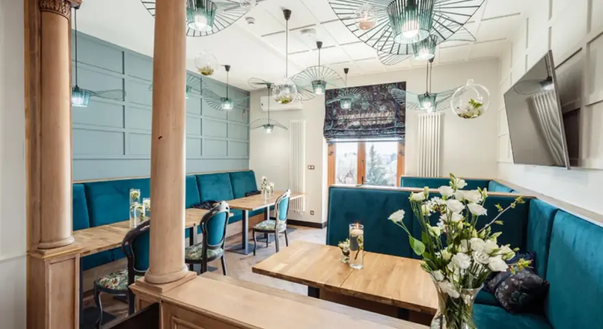 Wnętrze restauracji z turkusowymi kanapami, drewnianymi stołami i ozdobnymi lampami.