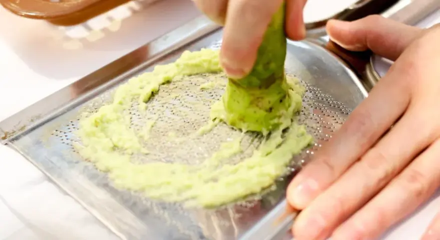 Świeże wasabi jest tarte na metalowej tarce, tworząc zieloną pastę. To właśnie tak powstaje prawdziwe wasabi.