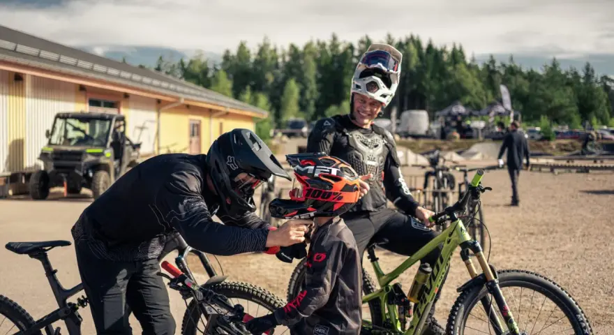 Två cyklister förbereder sig för mtb downhill. En vuxen hjälper ett barn med hjälmen.