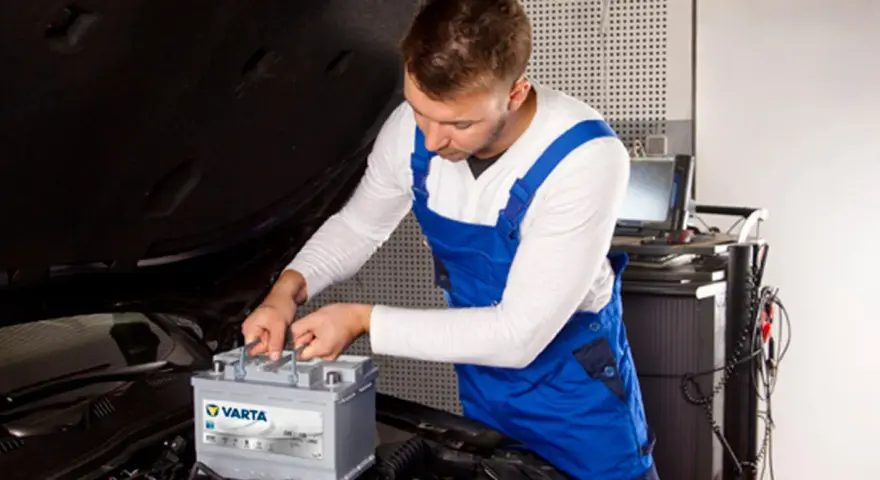 Mechanik w niebieskim kombinezonie wykonuje kodowanie akumulatora Varta w samochodzie.