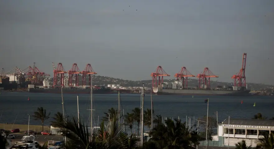 Port w Durban, RPA, z czerwonymi dźwigami portowymi i statkami towarowymi na tle wzgórz. Na pierwszym planie widać maszty jachtów.