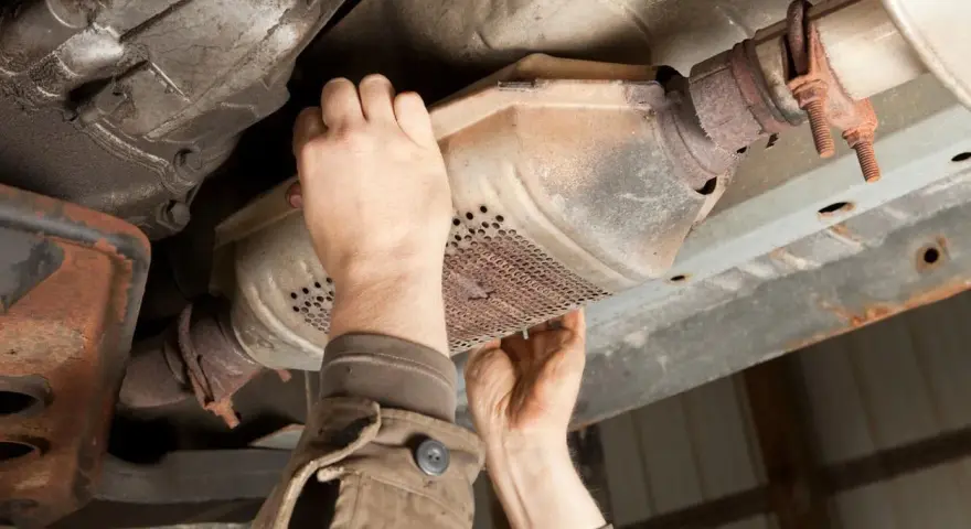 Mechanic inspecting a catalytic converter, a common culprit for why does my car smell like rotten eggs.