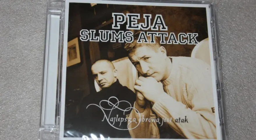 Okładka płyty "Peja Slums Attack - Najlepsza obrona jest atak". Dwóch mężczyzn, jeden w czarnym golfie, drugi w swetrze, spogląda wprost na widza.