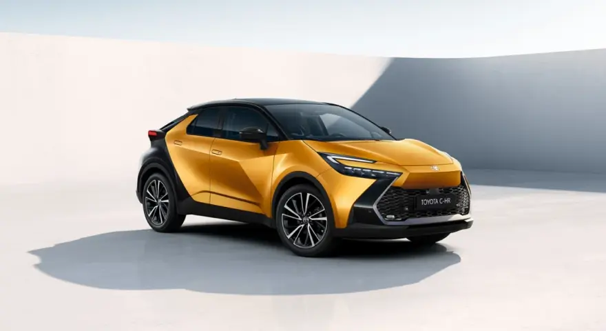 Nowy, złoty Toyota C-HR Hybrid z czarnym dachem prezentuje się dynamicznie na tle minimalistycznej architektury.