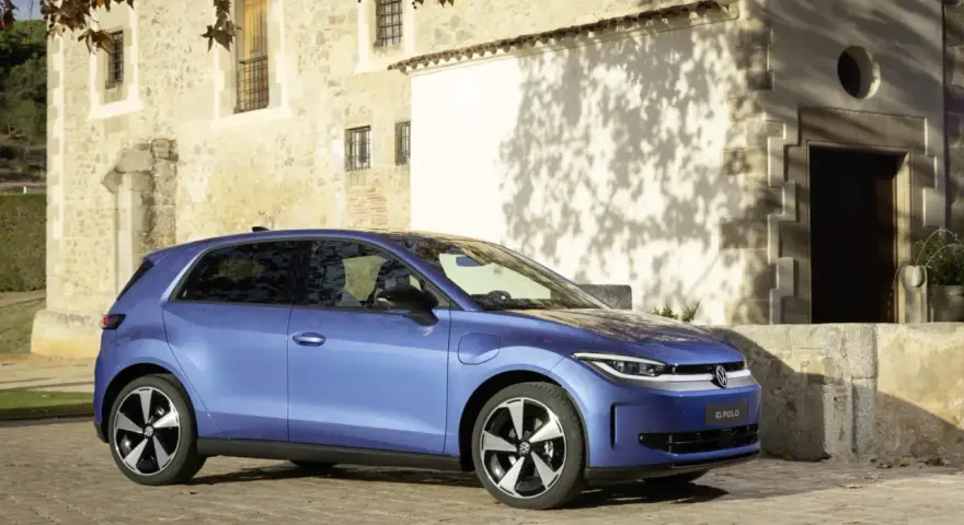Niebieski samochód elektryczny VW ID. Polo stoi na brukowanej drodze przed kamiennym budynkiem.
