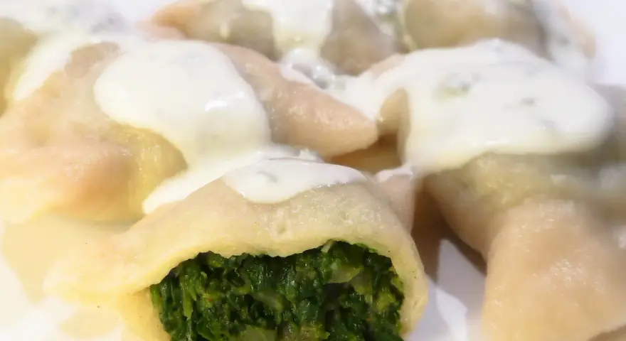 Pierogi ze szpinakiem polane sosem śmietanowym na białym talerzu.