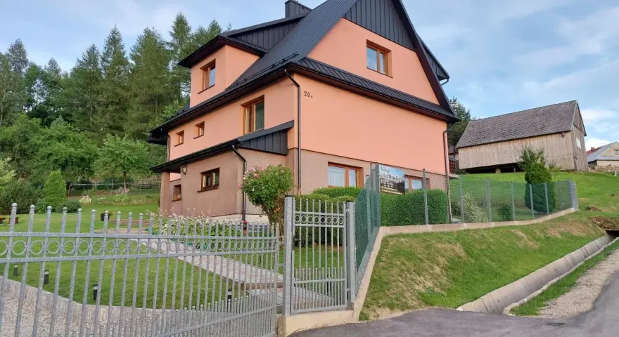 Urocze **mogielica schronisko** w otoczeniu zieleni. Jasnoróżowy budynek z czarnym dachem, obok drewniana stodoła.