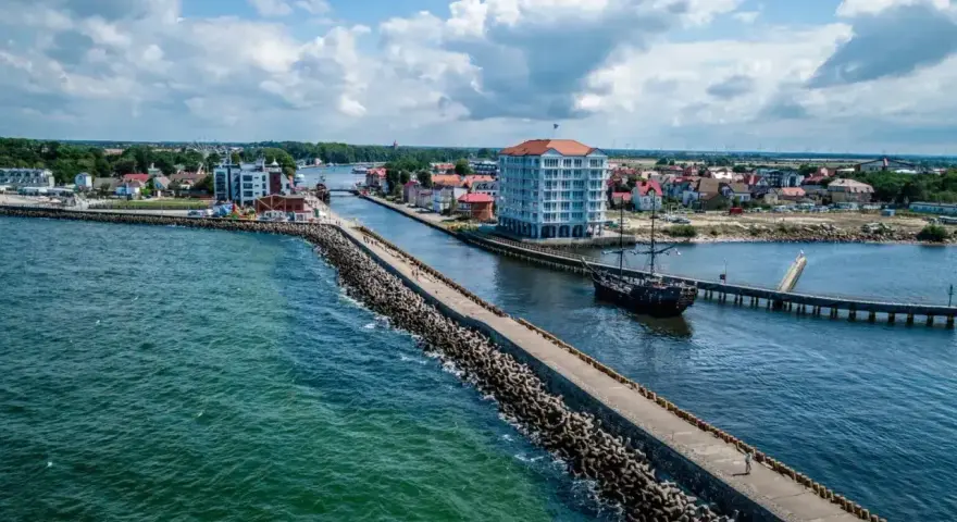 Widok na port w Darłówku z falochronem, statkiem pirackim i nowoczesnym budynkiem.