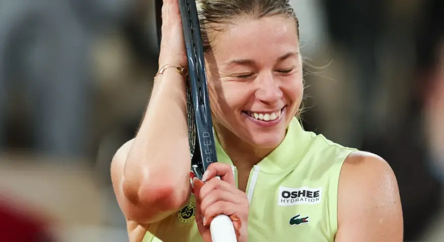 Szczęśliwa Iga Świątek, zwyciężczyni Roland Garros, z rakietą opartą o głowę, w geście triumfu.