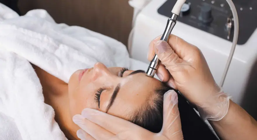 Aesthetician performs microdermabrasion on a woman's forehead. The question of microdermabrasion how often depends on skin type and goals.