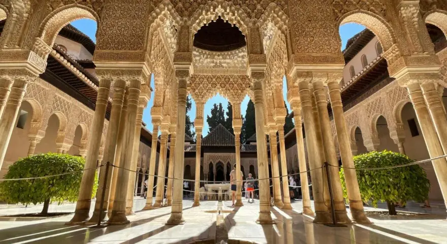 Intricate arches and columns of the Alhambra, a perfect postcard from Granada. Sunlight streams through, illuminating the detailed stonework.