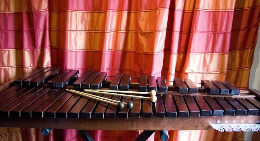 Ksylofon, instrument muzyczny na literę K, z pałeczkami, na tle czerwonej zasłony.