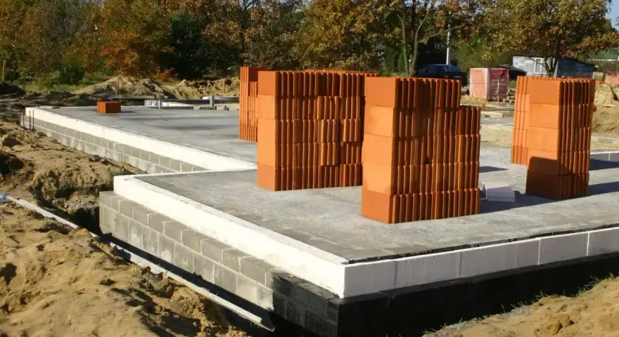 Budowa domu w toku. Stos pustaków i betonowa płyta fundamentowa. Zastanawiasz się, ile kosztują fundamenty?