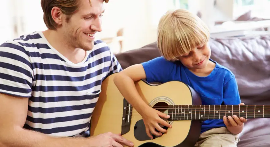 Ojciec uczy syna grać na gitarze. Radosna szkoła gry na gitarze w domowym zaciszu.