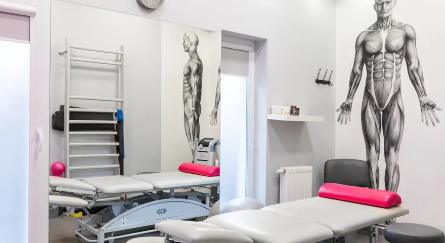 Gabinet rehabilitacyjny z leżankami, drabinką, piłką i aparaturą, w tym magnetronik na kolano.