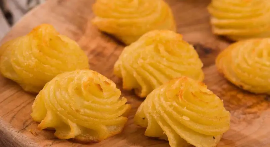 Patate duchessa dorate e invitanti, disposte su un tagliere di legno, pronte per essere gustate.