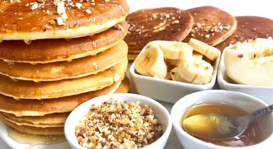 Pile de pancakes dorés arrosés de miel, accompagnés de rondelles de banane, de noix concassées et d'une cuillère de miel. Un délice pour le petit-déjeuner !