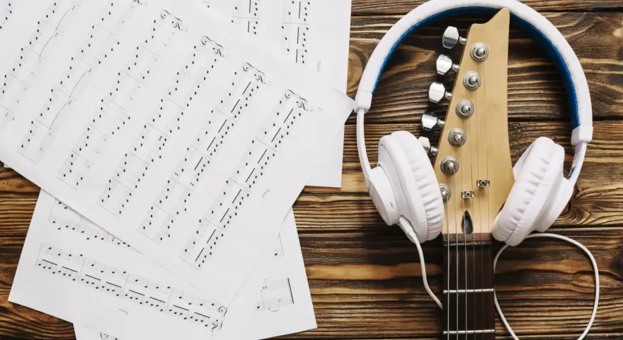 Nuty i gitara z białymi słuchawkami. Idealne do tego, by znaleźć piosenkę po nuceniu i stworzyć własną melodię.