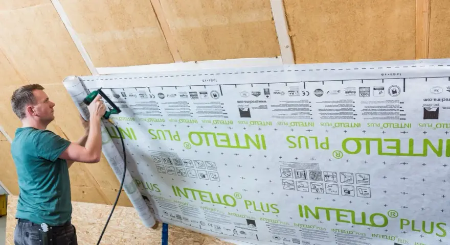 Mann bringt mit einem Tacker eine Dampfbremse an. Die Folie ist mit "INTELLO PLUS" bedruckt.