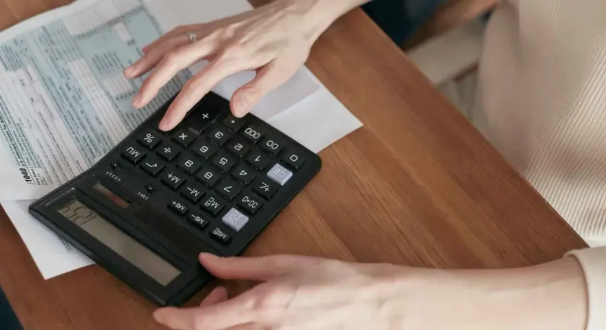 Manos calculando el total de suplidos en un formulario fiscal.