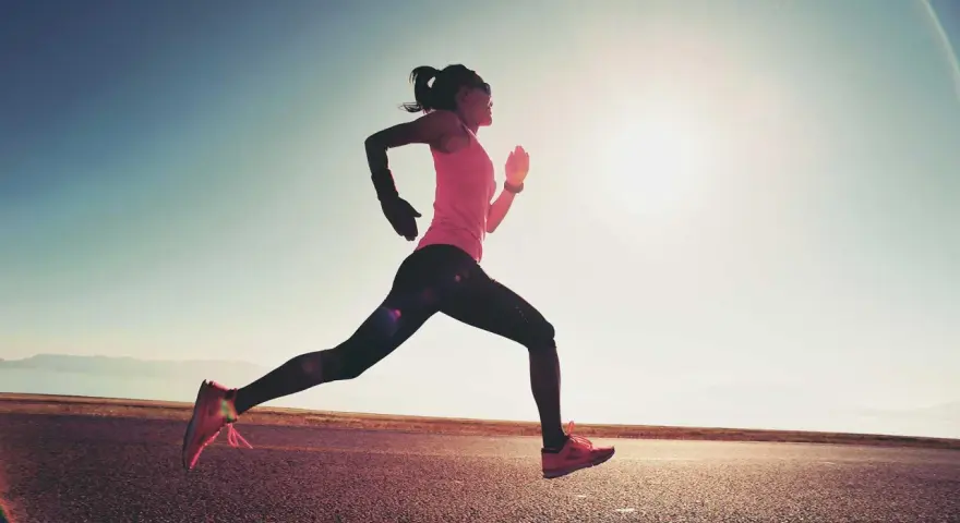 Donna corre su strada asfaltata al tramonto, con il sole che illumina la scena. Questo è un esempio di tempo run, un allenamento per migliorare la velocità.