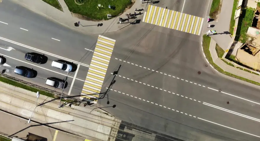 Vista aerea di un incrocio con strisce pedonali bianche e gialle. Auto in attesa nella corsia di preselezione, tram sui binari sottostanti.