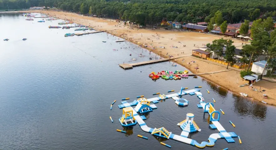Sielpia jezioro tętni życiem. Na piaszczystej plaży wypoczywają ludzie, a w wodzie szaleją na dmuchanych zjeżdżalniach i torach przeszkód.