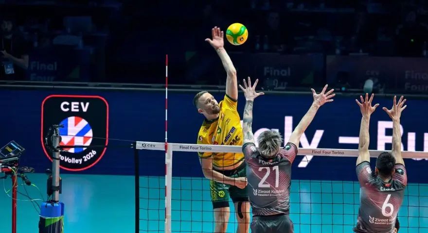Emocjonujący moment w final ligi mistrzów siatkówka. Zawodnik w żółtej koszulce atakuje, a dwaj gracze w szarych strojach próbują go zablokować.