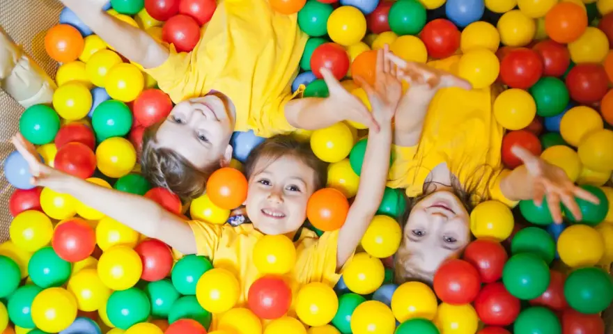 Drei Kinder in gelben T-Shirts spielen in einem Bällebad. Perfekte Ausflugsziele mit Kindern für Spaß und Lachen.