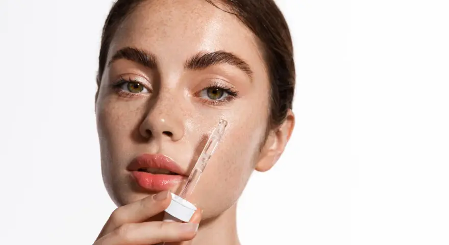 Kobieta aplikuje serum z pipetki na policzek. Skóra pełna piegów, nawilżona, z widocznym blaskiem. Kluczowe składniki: retinol i ceramidy.