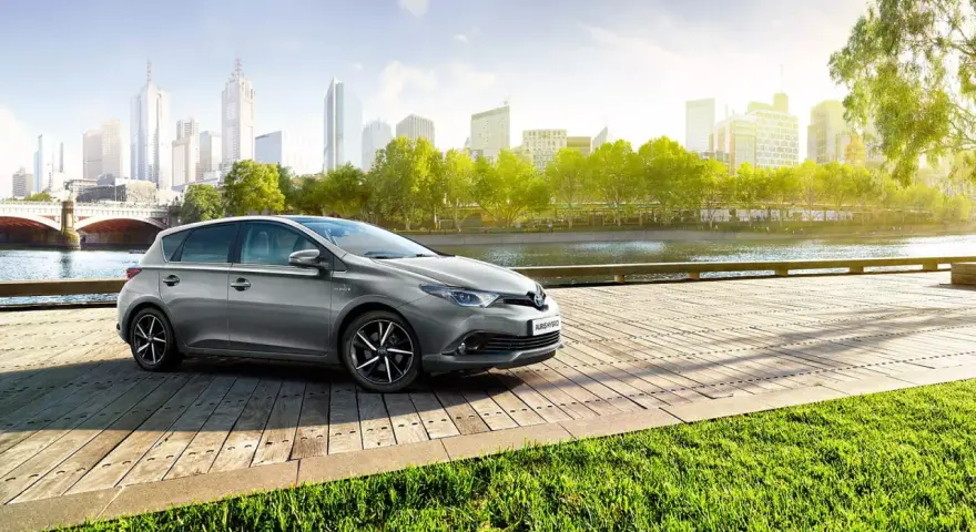 Szary Toyota Auris Hybrid na drewnianym pomoście, z miastem w tle. Jaki olej do tego modelu?
