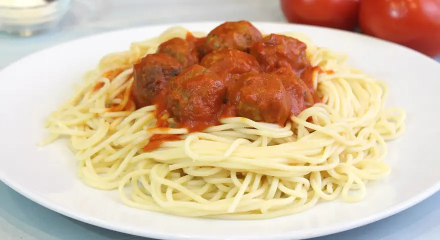 Un plato de espaguetis con albóndigas cubiertos de salsa roja.