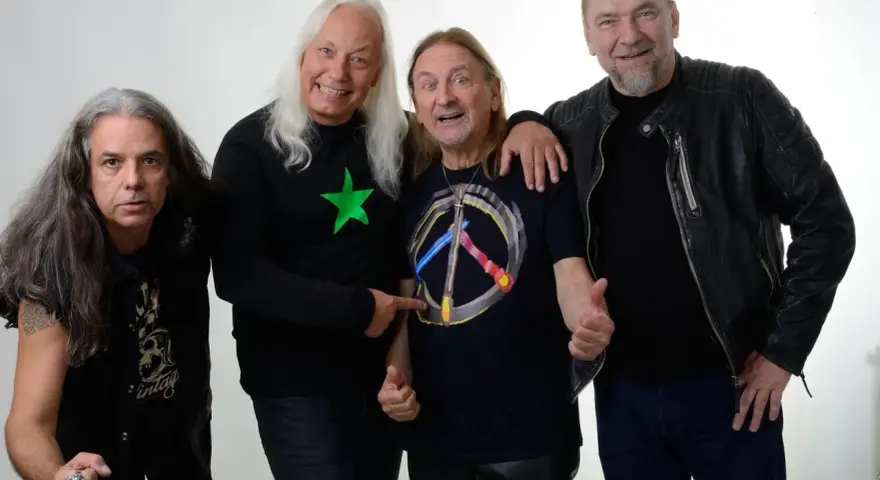 Czterech mężczyzn, TSA Dream Team, pozuje do zdjęcia. Dwóch z nich ma długie włosy, jeden w czarnej koszulce z zieloną gwiazdą, drugi w koszulce z symbolem pokoju.