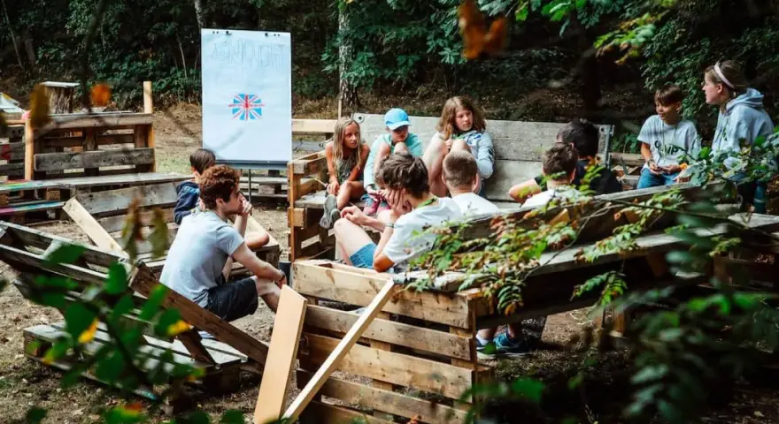 Kinder lernen im Freien beim englisch camp. Eine Tafel mit der britischen Flagge steht im Hintergrund.
