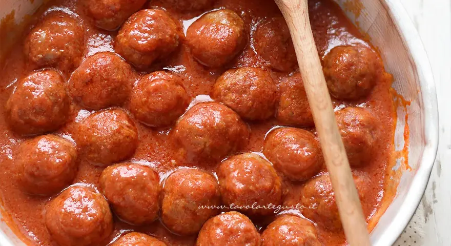 Polpette al sugo fumanti in una ciotola, pronte per essere gustate. Un cucchiaio di legno le accompagna.