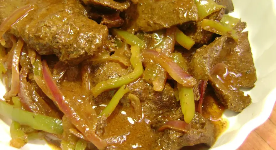 Hígado guisado con cebolla y pimientos verdes en salsa marrón.