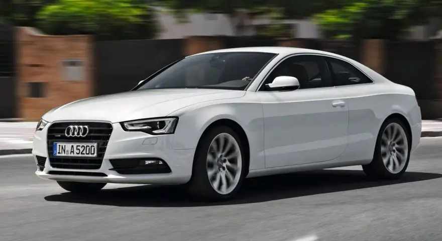 Białe Audi A5 Coupe pędzi po drodze, jego sylwetka jest dynamiczna i elegancka.