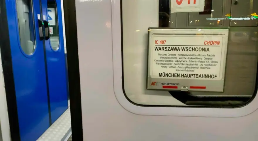 Tabliczka z rozkładem jazdy pociągu IC 407 Chopin na tle niebieskich drzwi pociągu.