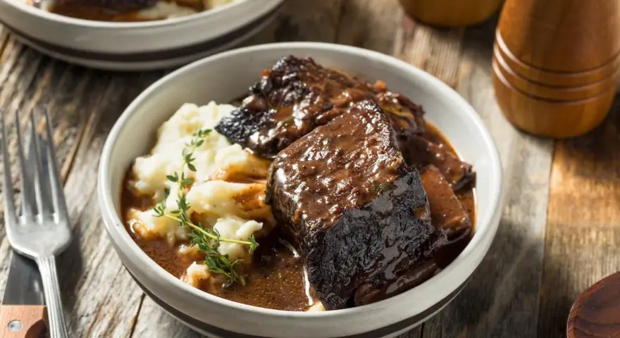 Un succulento girello di manzo brasato, tenero e saporito, servito su un letto di purè di patate cremoso, guarnito con rametti di timo fresco.