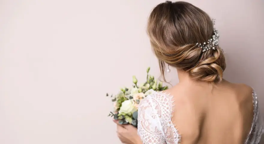 Eleganckie wesele: wlosy podpiete z jednej strony, ozdobione perłami, z bukietem kwiatów w dłoni.