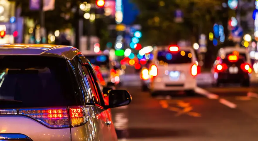 Luci sfocate e colorate in una strada trafficata di notte, come vedono i miopi le luci. Un'auto argentata in primo piano.