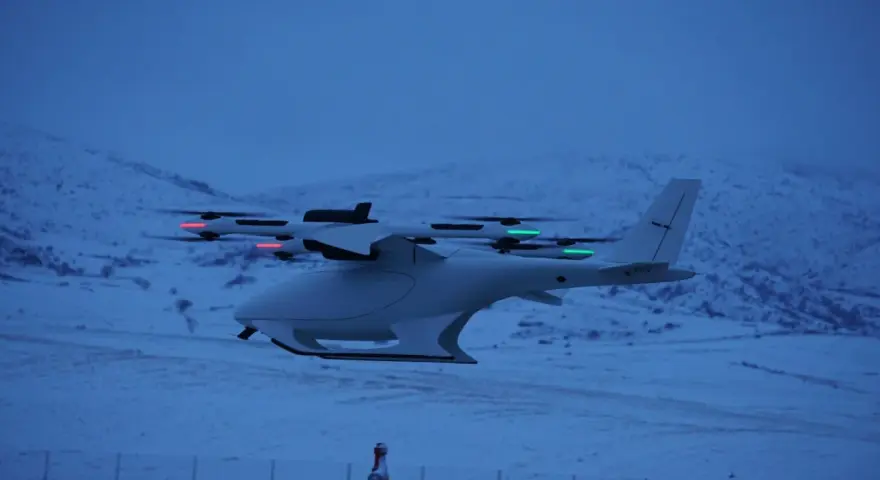 A white vtol drone with red and green lights flies over a snowy landscape at dusk.